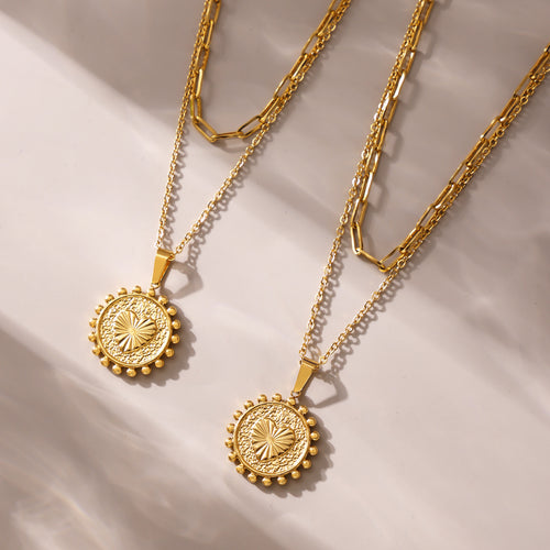 Two gold heart medallion pendants with paperclip chains on fabric