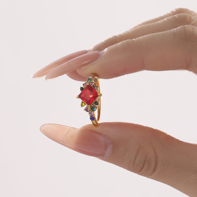 Hand holding gold ring with red multicolor zircon accents