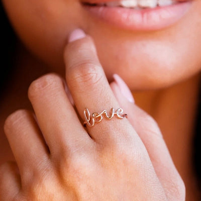 Rose gold love script ring worn on smiling model fingers