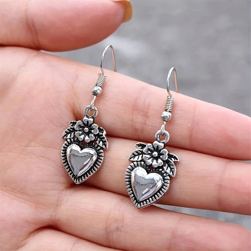 Pair of oxidized heart flower drop earrings resting on open palm