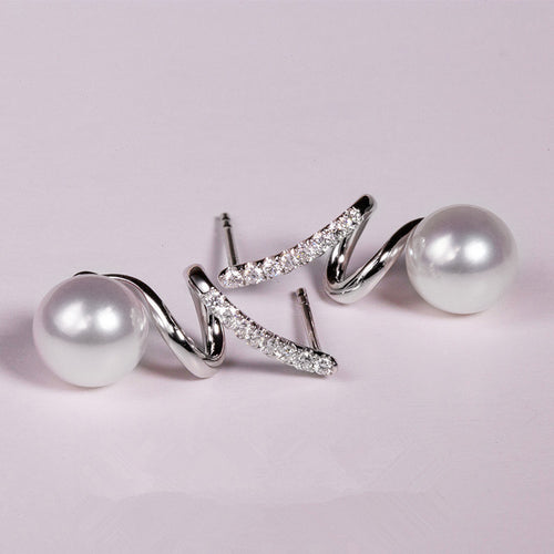 Silver spiral twist pearl studs lying on pale pink surface