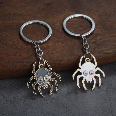 Black and white skull spider keychains with googly eyes displayed together on wood.