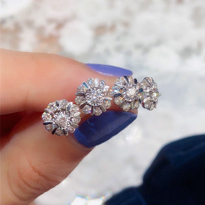 Four silver flower clear CZ cluster stud earrings held on fingertips