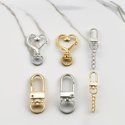 Six gold-tone and silver-tone swivel clasps arranged on a white marble surface.