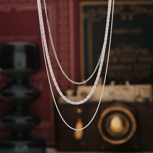 Steel triple chain necklace hanging before books and camera