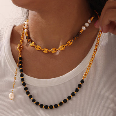 Model wearing stacked gold tiger-eye pearl and black bead necklaces