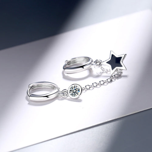 Silver linked star and clear stone huggies resting on white surface