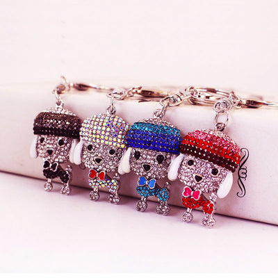 Four rhinestone dog keychains in black, iridescent, blue, and pink colors are displayed together.