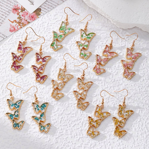 Six pairs of gold triple-butterfly pressed flower resin earrings on white cloth