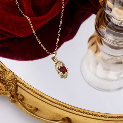 Gold pixiu red stone pendant necklace hanging over gold mirror frame
