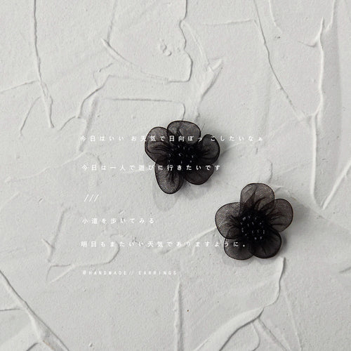 Pair of black mesh flower stud earrings on white textured surface