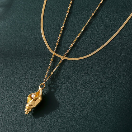 Gold conch shell pearl pendant with snake chain on dark surface