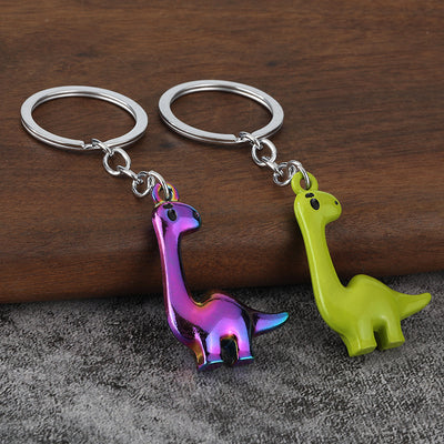 Two long-neck dinosaur keychains in iridescent purple and bright green finishes on a wooden surface.