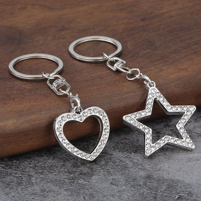 A heart-shaped and a star-shaped silver-tone keychain rest side by side on a dark surface.
