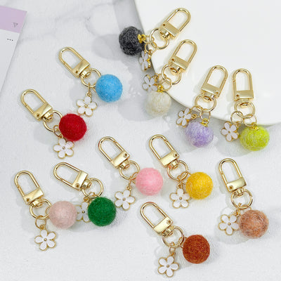 Assortment of felt ball keychains in many colors, each with a white flower charm and gold clasp