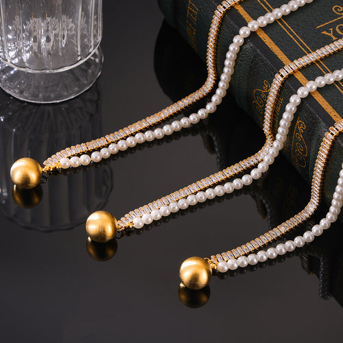 Three gold zircon pearl split necklaces with ball pendants on dark glass
