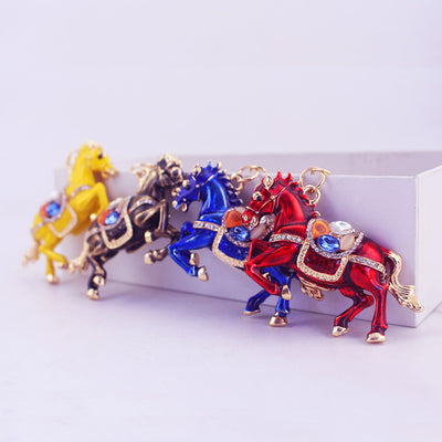 Four decorated horse charms in yellow, black, blue, and red are arranged beside a white block.
