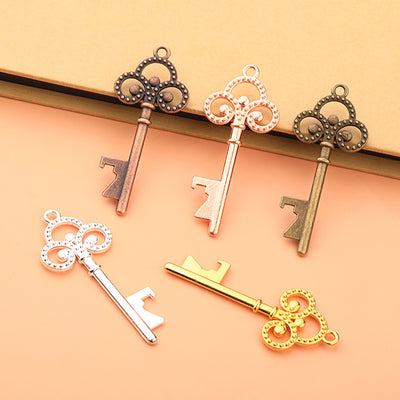 Five ornate key-form bottle openers in different finishes are arranged on a peach surface.