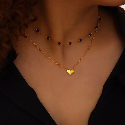 Model wearing gold double-layer necklace with blue beads and heart pendant