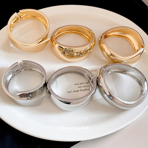 Six gold silver polished round and hinged bangles on white plate