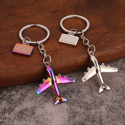 Silver and rainbow airplane keychains displayed together on a wood and gray surface.