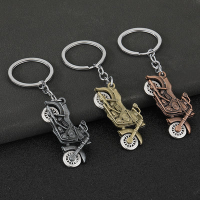 Three antique-finish motorcycle keychains on a dark backdrop