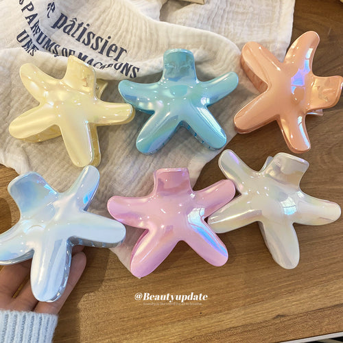 Six iridescent starfish acrylic claw clips in mixed pastel colors on wood