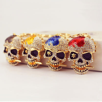 Four gold-tone rhinestone skull keychains with black, gold, blue, and red textured panels.