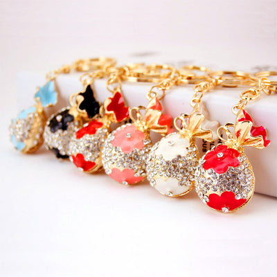 A row of six colorful purse-shaped keychains shows clear rhinestone and floral details.