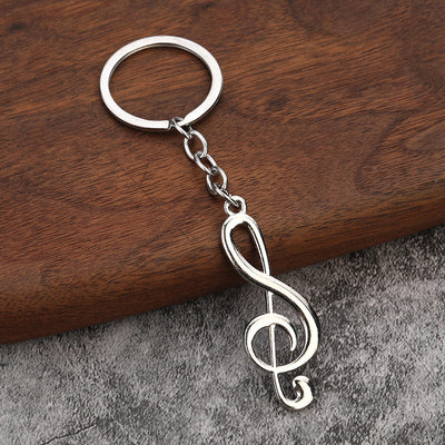 Silver-tone treble clef keychain resting on wood and gray fabric.