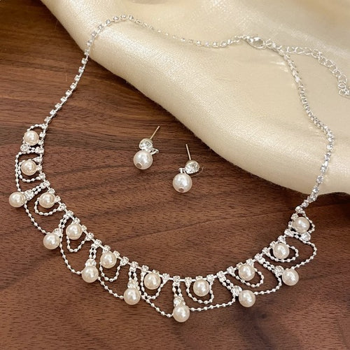 Silver pearl fringe necklace and stud earrings laid on dark wood table
