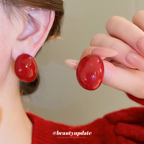 Second listing image of glossy red oval stud earrings, showing the visible finish.