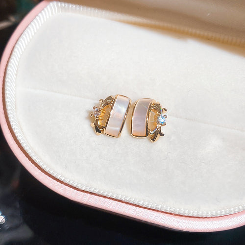 Compact gold tone geometric studs with pale rectangular centers shown in a styled front view.