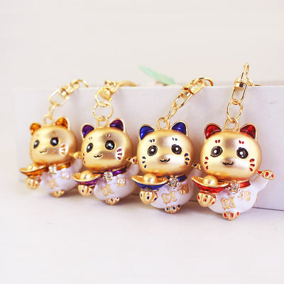 Four gold-tone lucky cat keychains with gold, purple, blue and red accents.