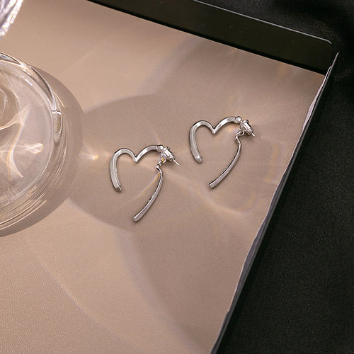 Silver open heart stud earrings with hanging bars on beige tray