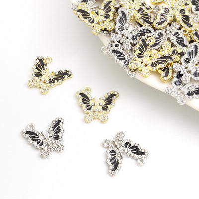 Assorted black enamel crystal butterfly charms arranged beside a tray on white