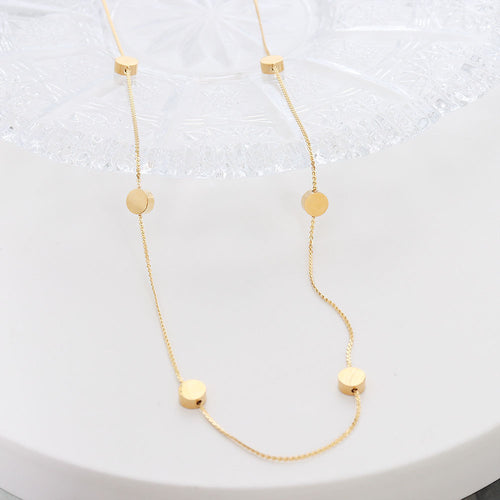 Close-up of gold spaced flat disc beads on fine chain over crystal plate