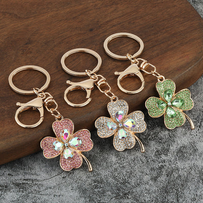 Three gold-tone four leaf clover keychains in pink, white, and green rhinestone styles.