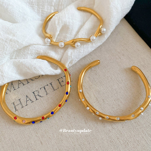 Three gold open cuff bangle styles arranged on fabric and paper