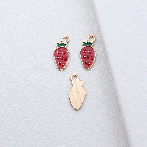 Pink strawberry enamel charm arranged on a natural wood surface