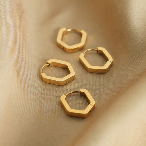 Four gold hexagon hoop earrings scattered on champagne satin