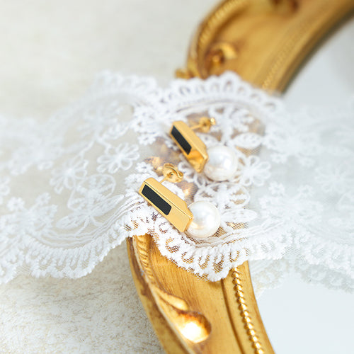 Gold black-inlay bar pearl stud earrings on lace over ornate gold mirror