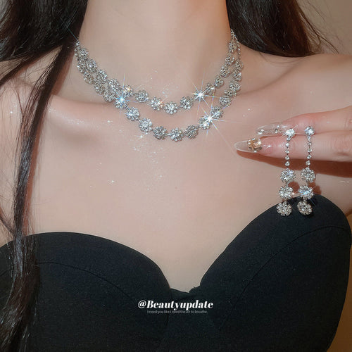 Silver rhinestone flower necklace worn with matching dangling earrings held in hand