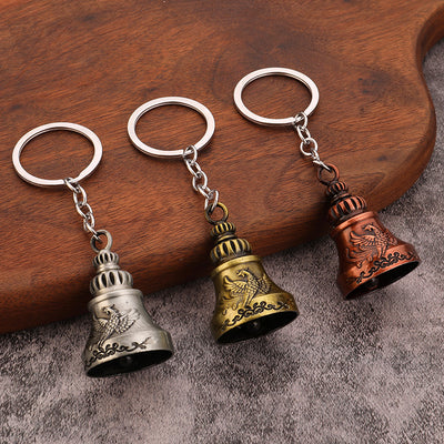 Three bell keychains in silver, brass, and copper tones arranged on a wooden surface.