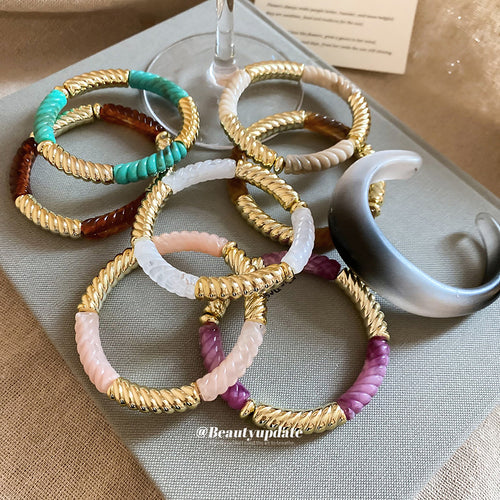 Group of twisted rope acrylic gold bracelets beside wine glass and cuff