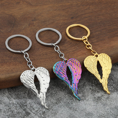 Gold, silver, and iridescent heart wing keychains arranged on wood.