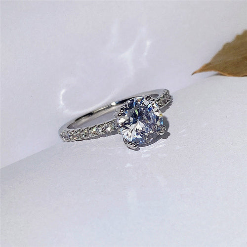Silver round clear stone ring on white surface with leaf accent