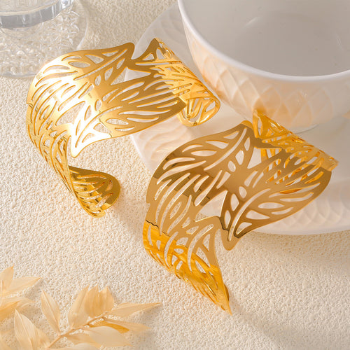 Two gold leaf-cut open bangles displayed beside white cup and glass