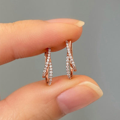 Close finger-held view of rose gold X pave huggie pair