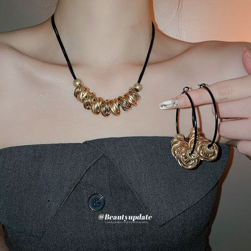 Gold twisted circle black cord necklace worn with matching hoops held